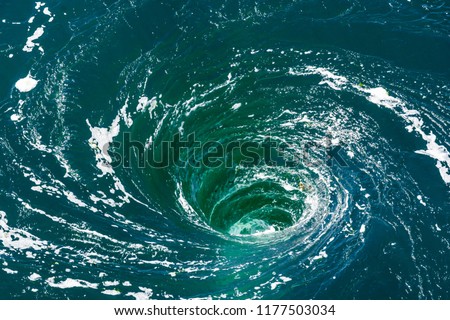 High angle view of a powerful whirlpool at the surface of green water with foam.