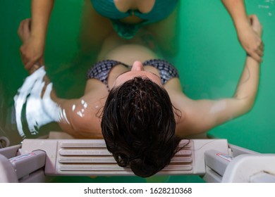 High angle view of pregnant woman resting on ladder in bikini while woman therapist holding hand and giving hydrotherapy in swimming pool - Powered by Shutterstock