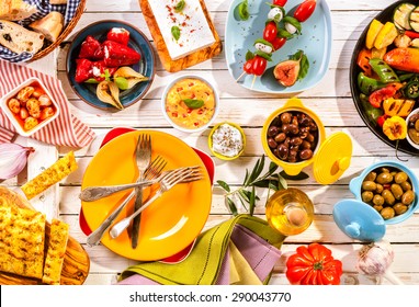 High Angle View of Prepared Colorful Mediterranean Meal Spread Out on Painted White Wooden Picnic Table with Bright Plates and Cutlery
