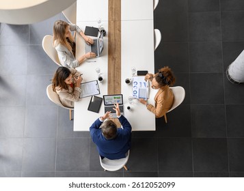 High angle view of professionals analyzing business reports over laptops and documents on table in meeting