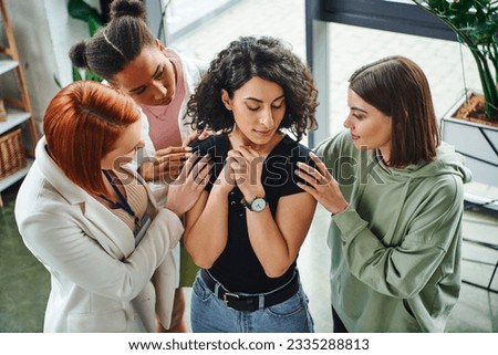 high angle view of psychologist and multiethnic female friends calming frustrated multiracial woman standing with closed eyes in consulting room, moral support and mental wellness concept