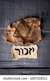 high angle view of a ragged jewish badge and a yellowish piece of paper with the word yizkor, remember in hebrew and the name of a prayer in memory of deceased beloveds, on a rustic wooden surface