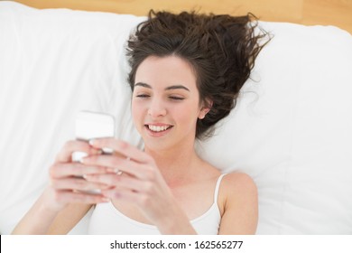 High angle view of a relaxed young woman text messaging in bed at home