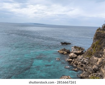 High Angle View of Rocky Cliffside and Clear Turquoise Ocean Water Under Overcast Sky