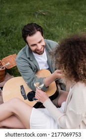 High Angle View Of Romantic Man Playing Acoustic Guitar Near Curly Woman With Glass Of Wine
