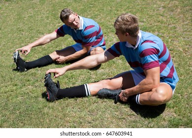 High angle view of rugby players stretching while sitting on grassy field - Powered by Shutterstock