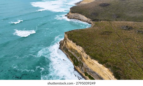 High angle view of rugged limestone cliffs meeting turquoise ocean waves along the coastline.