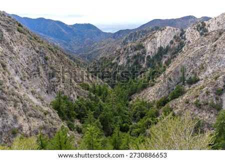 High angle view of the rugged San Gabriel Mountains featuring steep rocky slopes and a dense evergreen forest canyon in Angeles National Forest, California.