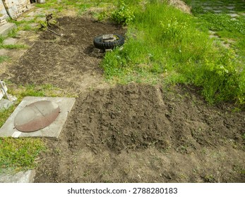 High angle view of a rural backyard garden with dug up soil patches, a metal manhole cover, and an old tire.