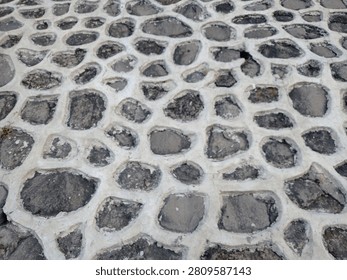 High angle view of rustic cobblestone pavement texture with wide white concrete mortar joints creating a distinct repeating web pattern.