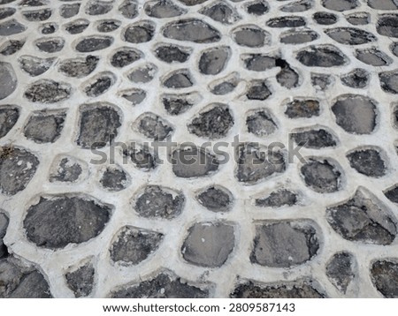 High angle view of rustic cobblestone pavement texture with wide white concrete mortar joints creating a distinct repeating web pattern.