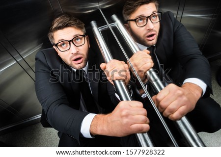 high angle view of scared businessman in suit with claustrophobia sitting on floor in elevator