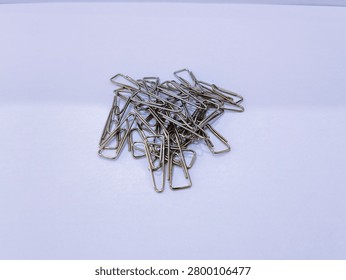 High angle view of scattered metallic paper clips on white surface, essential stationery for school and office work