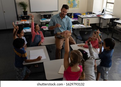 High angle view of school kids raising hands while teacher studying in classroom of elementary school