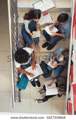 High angle view of high school students group sitting on staircase and studying together for next exam. Top view of young group of classmates doing homework sitting on college staircase.