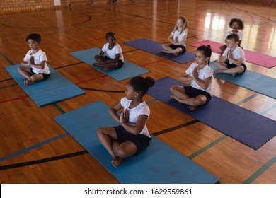 High angle view of schoolkids doing yoga and meditating on a yoga mat in school with crossed legs - Powered by Shutterstock