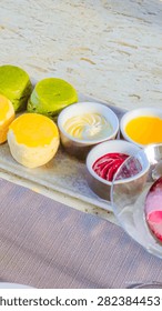 A high angle view of a selection of colorful scones served with various jams, cream, and lemon curd on a serving tray.