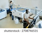 High angle view selective focus shot of African American man and Caucasian woman working in printing house preparing paper