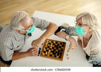 High angle view of senior couple with protective face masks elbow bumping while playing chess during coronavirus epidemic. - Powered by Shutterstock