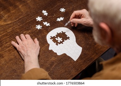 Hochwinkel-Ansicht des Seniors, der das Puzzle als Demenz-Rehabilitationsmaßnahme sammelt