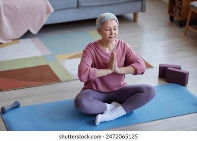 High angle view at serene senior woman with eyes closed meditating at home during yoga practice copy space - Powered by Shutterstock