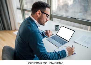 High angle view of serious businessman writing notes in diary. Male executive is using laptop while working at desk. White blank clean empty mock up template background computer laptop screen. - Powered by Shutterstock