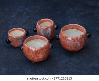 High angle view of a set of four handcrafted red glazed ceramic succulent pots. Assorted hand-built pottery planters with unglazed interior and decorative black handles on a dark textured background.
