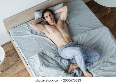 high angle view of shirtless man lying in bed with hands behind head