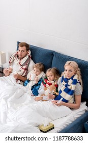 High Angle View Of Sick Young Family Sitting In Bed Together And Looking At Camera