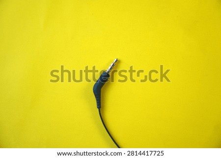 High angle view of a single black 3.5mm TRRS audio jack connector with a gold-plated tip and a black cable, isolated on a vibrant yellow background. Concept of sound hardware, auxiliary input, and music technology connection.