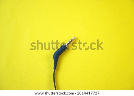 High angle view of a single black 3.5mm TRRS audio jack connector with a gold-plated tip and a black cable, isolated on a vibrant yellow background. Concept of sound hardware, auxiliary input, and music technology connection.