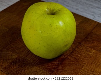 High angle view of a single ripe green apple resting on a rustic wooden cutting board, symbolizing natural food preparation, organic ingredients, and kitchen still life.