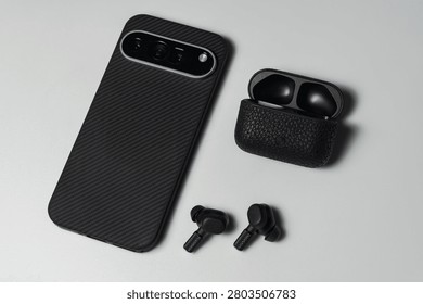 High angle view of a sleek mobile phone in protective case beside open leather textured earphone box on white table surface.