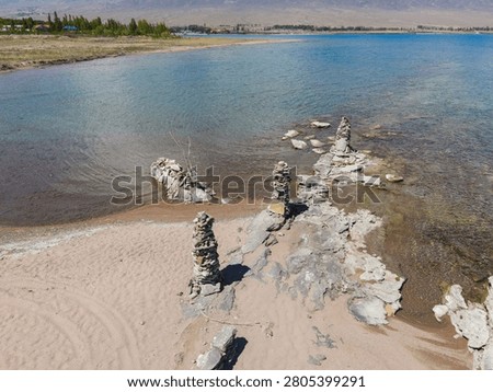 High angle view of small manmade stone towers stacked carefully on the rocky and sandy shore of clear Issyk Kul Lake