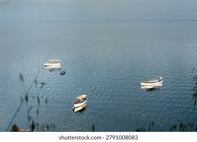 High angle view of small passenger boats floating on a vast blue lake surface.