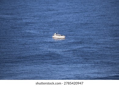High angle view of a small white boat sailing alone across the vast and deep blue ocean surface.