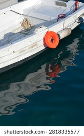 A high angle view of a small white wooden boat with an orange ring buoy and its clear reflection in the calm blue sea water.