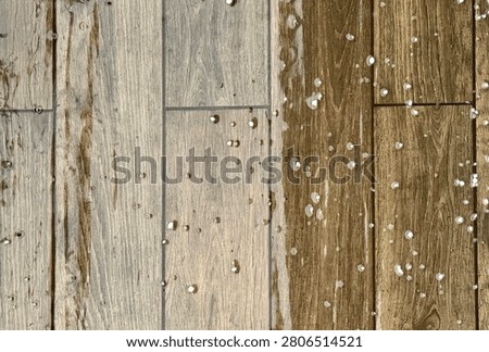 High angle view of small white hailstones and raindrops scattered across a wet wooden-textured tiled floor during a storm.