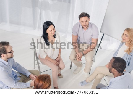 high angle view of smiling multiethnic middle aged people sitting on chairs and talking during group therapy