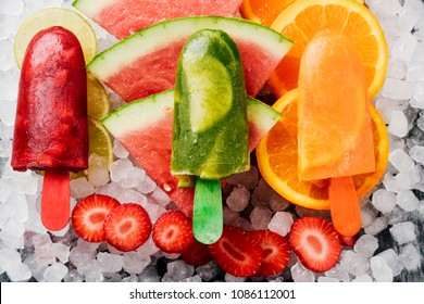 high angle view of some different homemade ice pops, made with different natural fruit juices and pieces of fruit, such as watermelon, strawberry, peach, lime or orange, placed on ice - Powered by Shutterstock