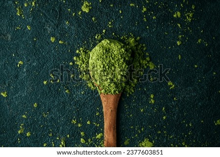 high angle view of some matcha powder tea in a wooden spoon placed on a dark textured stone surface
