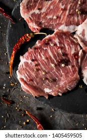 high angle view of some pieces of raw secreto iberico, a pork cut from spanish iberian pig, on a black slate tray, placed on a gray stone table or countertop
