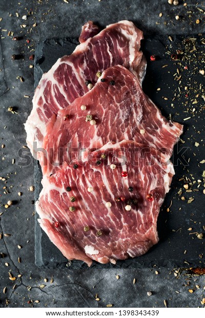 high angle view of some pieces of raw\
secreto iberico, a pork cut from spanish iberian pig, on a black\
slate tray, placed on a gray stone table or\
countertop