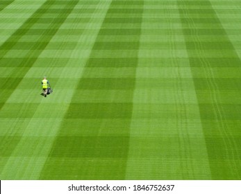 A high angle view of a sports ground covered by green grass on a sunny day being mowed by a groundskeeper in square pattern - Powered by Shutterstock