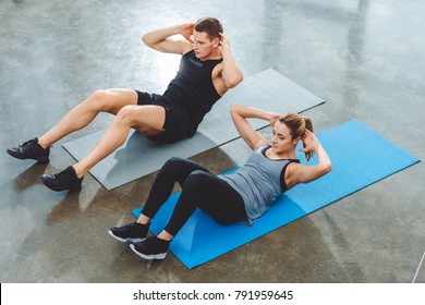 High Angle View Of Sporty Young Couple Doing Abs Exercise In Gym