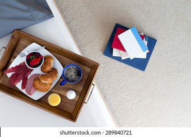 High Angle View of Stack of Books on Floor Beside Bed with Breakfast in Bed Tray on Top with Assortment of Food