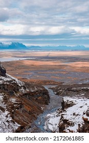 High angle view of stream flowing amidst snow covered mountains. Idyllic scenery of rock formations in volcanic valley. Scenic view of winter landscape against cloudy sky.