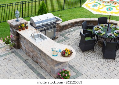 High angle view of a stylish outdoor kitchen, gas barbecue and dining table set for entertaining guests with formal place settings and flowers on a paved patio - Shutterstock ID 262125053