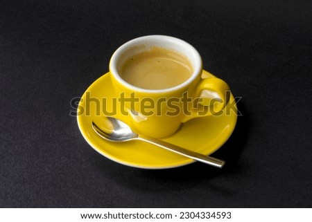 High angle view of sun flower yellow espresso cup with saucer and silver colored spoon against black background. Photo taken May 17th, 2023, Zurich, Switzerland.