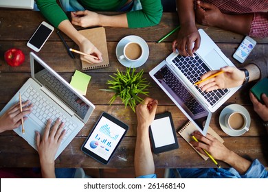 High angle view of table and people sitting at it with laptops and touchpads